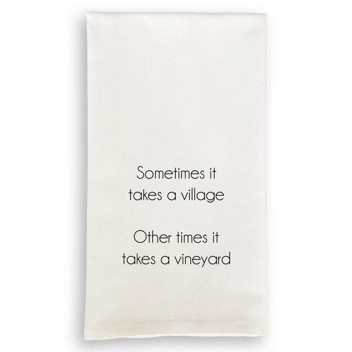 White cotton tea towel with black text reading "Sometimes it takes a village. Other times it takes a vineyard."
