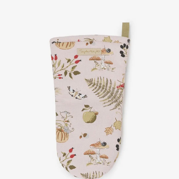 A light TAUPE  oven mitt with an autumn-themed print featuring mushrooms, ferns, acorns, and leaves, complete with a small olive green tab at the top and a fabric brand label.