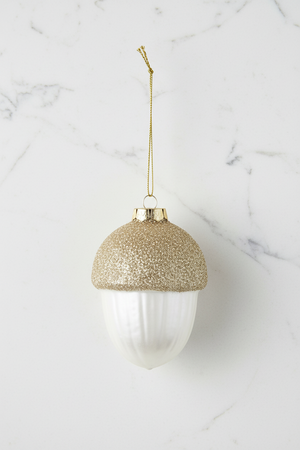 Acorn-shaped Christmas ornament with a glittery gold cap and a ribbed white body, hanging from a gold string on a white background.