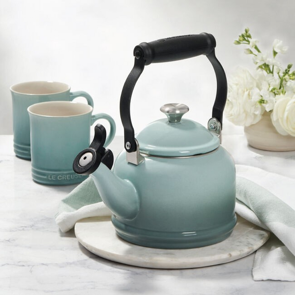 Sea Salt Le Creuset kettle with black handle and two matching mugs on a marble surface with white flowers in the background.