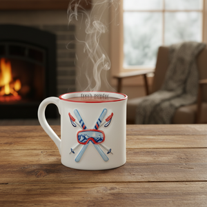 A white ceramic coffee mug with a red rim, featuring a 3D-effect graphic of crossed skis, ski poles, and ski goggles with blue mountains inside. The words 'fresh powder' are printed in black on the inside of the mug.