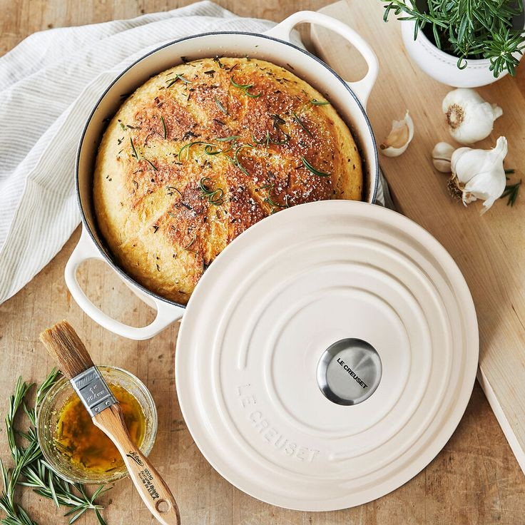A Artichaut Le Creuset enameled cast iron Dutch oven with a matching lid, displayed on a dark metal pedestal against a dark background.