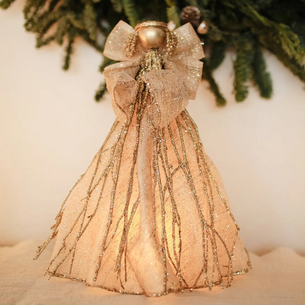 Handmade sinamay angel tree topper with a glittered cone-shaped gown and wings, gold twigs, and a gold halo, glowing softly from a flameless candle inside.