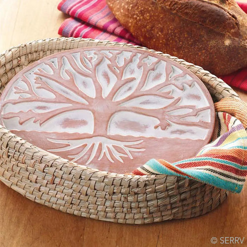 Decorative ceramic plate with tree design on a woven tray with bread and colorful napkins.