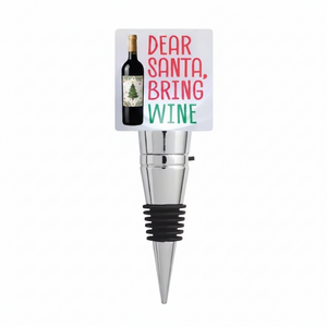 A wine bottle stopper with a white square insert featuring the text 'DEAR SANTA, BRING WINE' in red and green, alongside an illustration of a wine bottle. The stopper has a shiny silver metal body and a black rubber seal at the bottom.