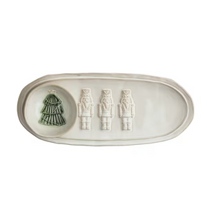 An off-white ceramic holiday serving tray with a small round dish containing a green Christmas tree, alongside three embossed nutcracker figures, shown on a plain white background.