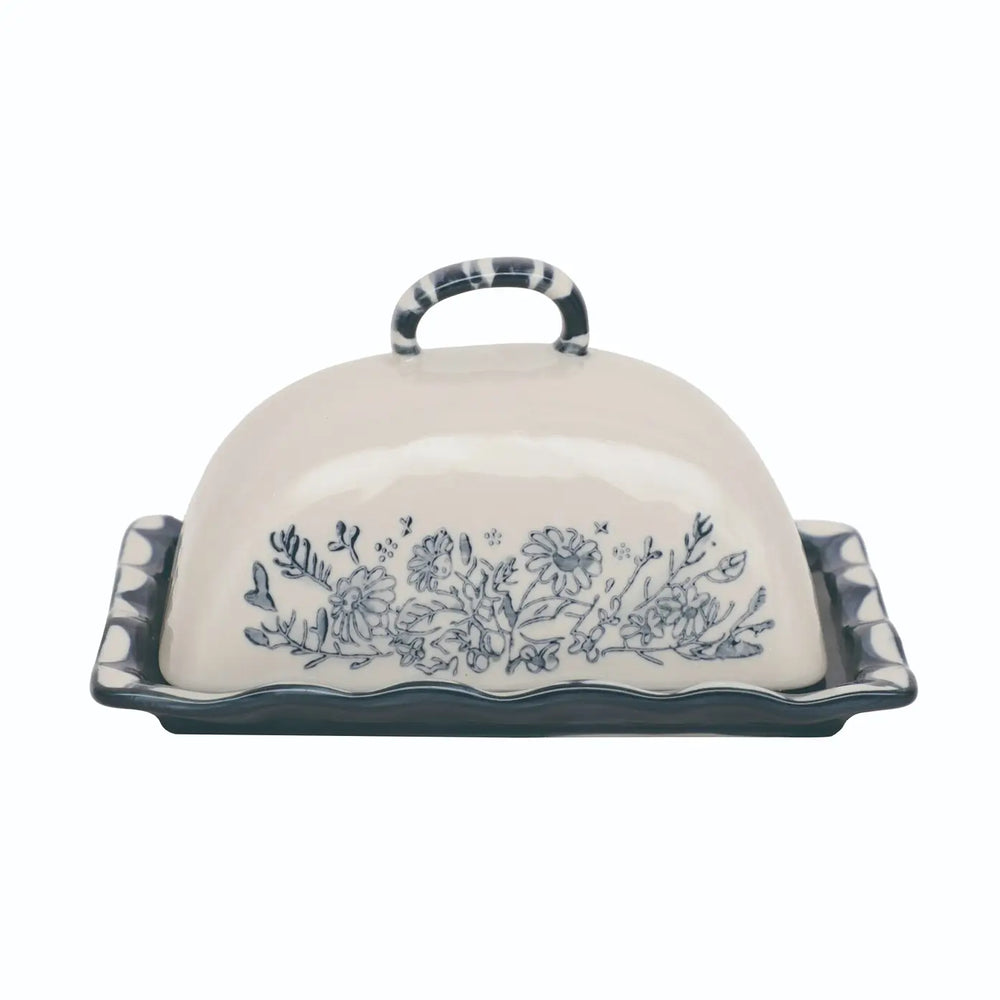 A ceramic butter dish with a domed lid, featuring a blue floral pattern on the front and a dark blue scalloped rim with a matching handle, set against a plain white background.