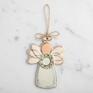 A hand-painted angel Christmas ornament with a light green dress, pale peach head, translucent wings, and a green wreath with red berries, hanging from a twine loop.