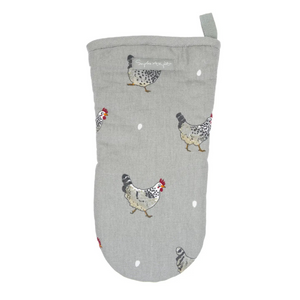 A single oven mitt in a muted sage green color, printed with a pattern of black-and-white speckled chickens and small white dots, laid flat on a white marble surface.