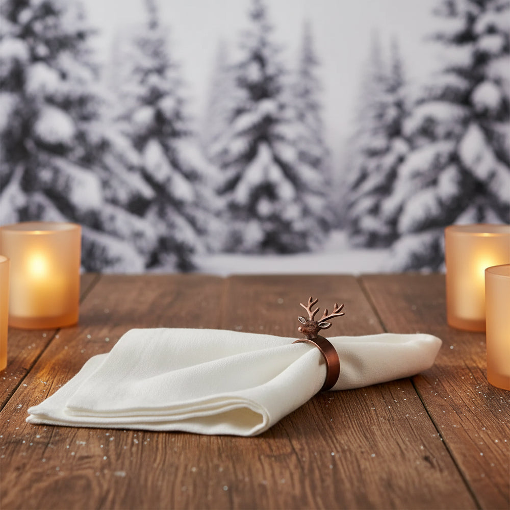 An off-white linen napkin folded into a diamond shape and secured with a bronze reindeer ring holder, set against a plain light gray background.