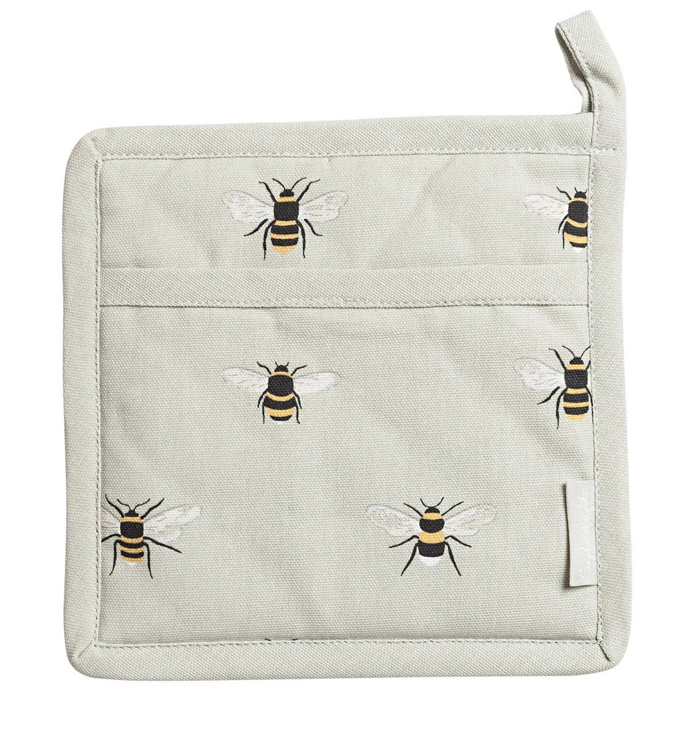 A square kitchen pot holder with  bumblebees, hanging from a metal hook on a kitchen shelf next to a wooden spoon.