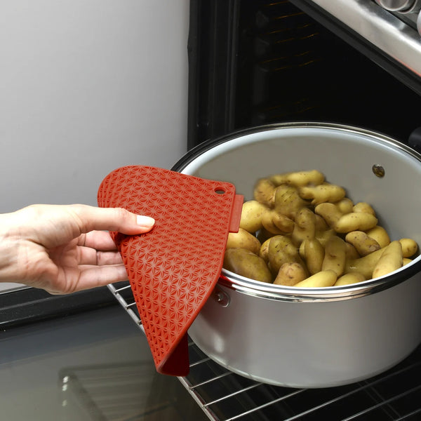Person holding a red silicone oven mitt over a pot of potatoes in an oven.
