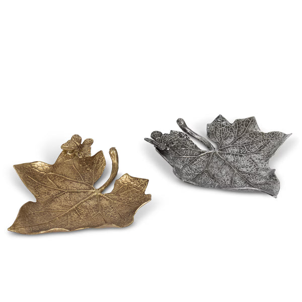 Two leaf-shaped decorative objects on a plain white background, one in metallic gold and one in metallic silver, both with textured veining and curled leaf edges.