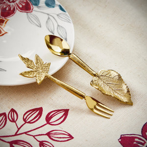 Gold leaf-shaped spoon and fork set on a floral-patterned tablecloth