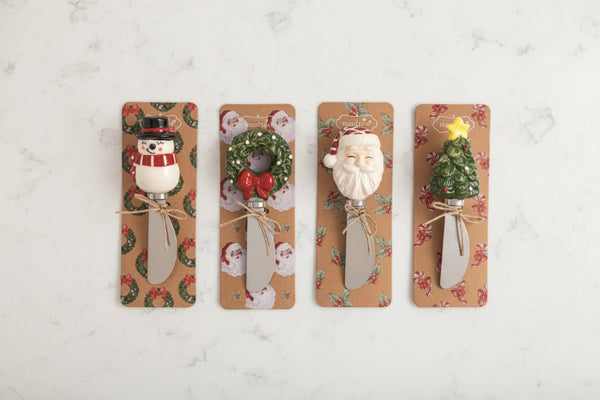 Four Christmas-themed decorative spreader handles mounted on tan patterned cards against a white background. The designs include a snowman, a wreath with a red bow, Santa Claus, and a Christmas tree with a yellow star.