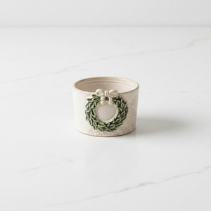 A small ceramic tidbit dish with a green wreath and bow design on a white marble surface.