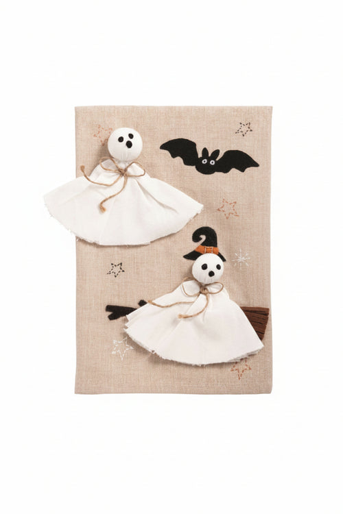 A beige linen tea towel with embroidered and appliqué Halloween designs, including two white ghost figures, a black bat, and a witch riding a broomstick, shown on a white background with a 'Click to zoom' overlay.