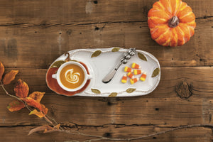 An autumn-themed ceramic serving platter with a pumpkin bowl and leaf accents, styled on a rustic wooden table with a small pumpkin, fall leaves, and candy.