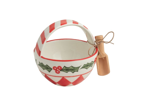 A ceramic Christmas-themed bowl with a red and white striped handle, green holly leaf and berry patterns, and a small wooden scoop tied to the side with twine, shown on a plain white background.