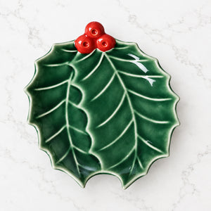 Holly-shaped ceramic plate with green leaves and bright red berries.