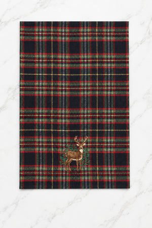 Black plaid woven kitchen towel with green, red, and yellow accents and an embroidered deer surrounded by holly leaves and red berries.