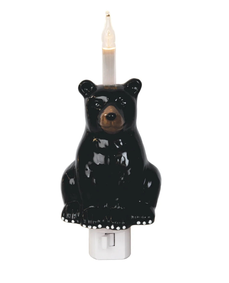 A black bear-shaped night light with a lit candle inside, mounted on a white plastic switch outlet, shown against a plain white background.