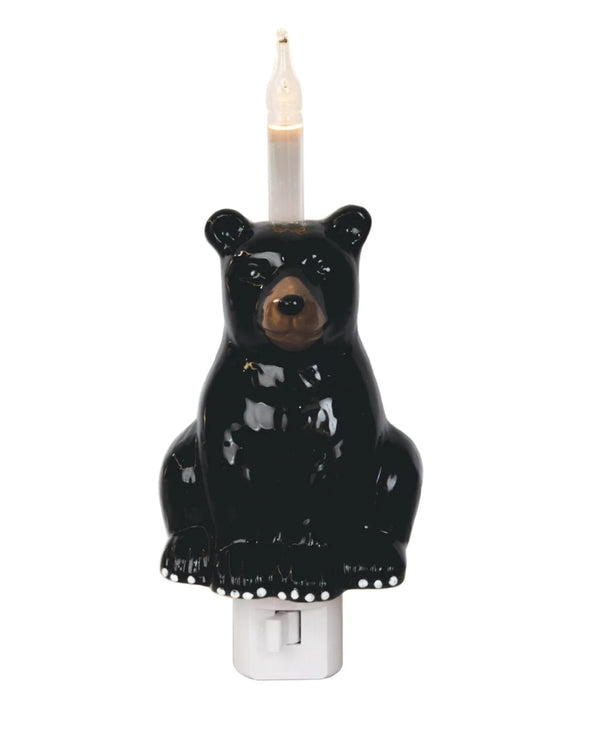 A black bear-shaped night light with a lit candle inside, mounted on a white plastic switch outlet, shown against a plain white background.