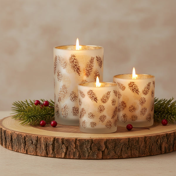 Three frosted glass taper holders in different sizes, decorated with a metallic gold pinecone pattern and featuring a shimmering gold interior, set against a plain white background.