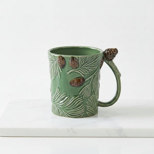 A green ceramic mug designed to look like a pine branch, featuring embossed pine needles, three raised pinecones on the body, and a pinecone attached to the handle, shown against a plain white background.