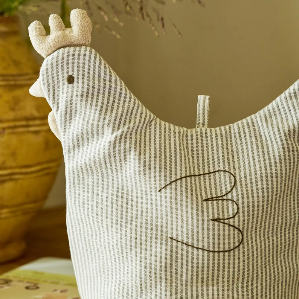 Striped chicken-shaped tea cosy on a wooden surface with a neutral background