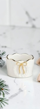 Aspen Kitchens Home+Gift stoneware tidbit bowl with a white scalloped edge and a gold bow motif for holiday serving.