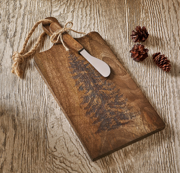 Mango wood charcuterie board with sketched evergreen tree artwork and a matching cheese spreader.
