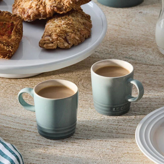 Two Le Creuset Espresso mugs on a wooden table with pastries in the background