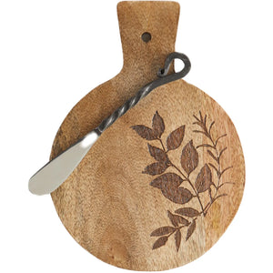 Round wooden serving board with a handle and engraved leaf pattern, shown with a metal spatula on a white background.