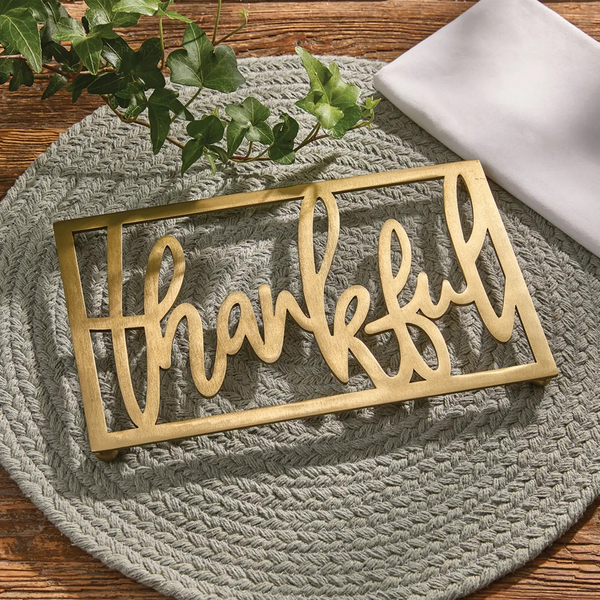 Rectangular brushed gold metal trivet with the word "thankful" in cutout script lettering.