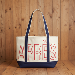 An off-white canvas tote bag with navy blue straps and bottom trim, featuring the word 'APRÈS' outlined in red on the front.