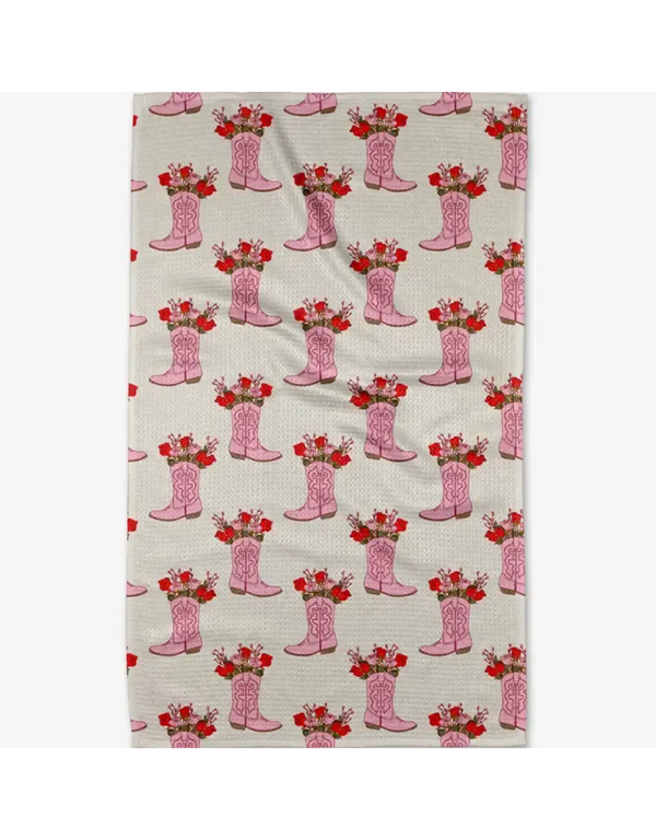 A rectangular fabric item, likely a tea towel or kitchen towel, featuring a repeating pattern of pink cowboy boots filled with red roses on a light beige background.