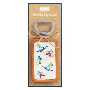 A bottle opener featuring a silver metal bottle opener attached to a rectangular canvas patch with colorful embroidered skiers, tied with twine and mounted on a brown kraft card.
