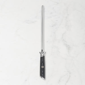 A vertical honing steel with a polished silver metal rod and a black textured handle, centered on a white marble background.