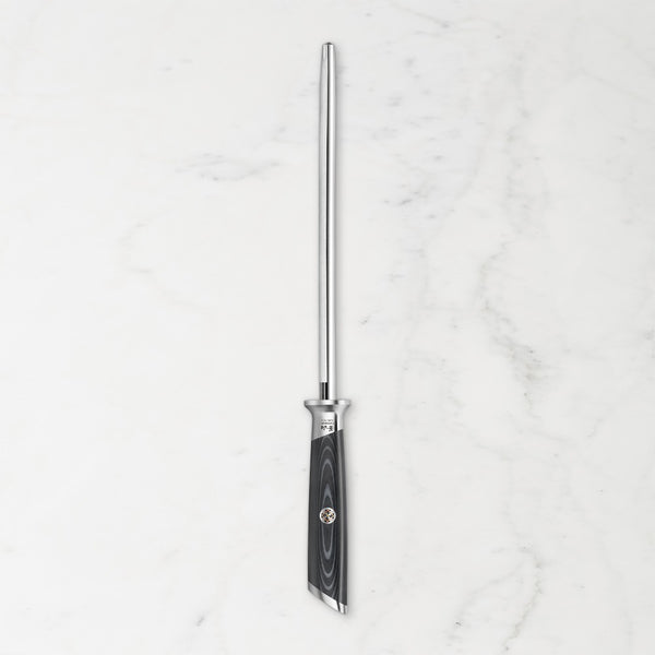 A vertical honing steel with a polished silver metal rod and a black textured handle, centered on a white marble background.