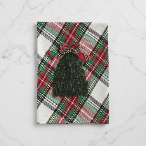 A rectangular kitchen towel with a red, green, and white plaid pattern, featuring a dark green tiered Christmas tree applique tied with a matching plaid bow at the top.