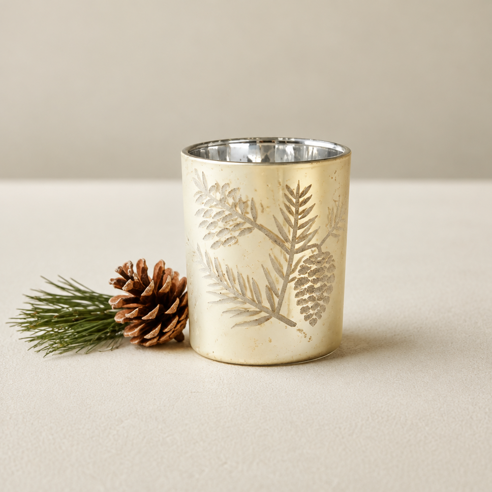 Gold glass votive candle holder etched with a pinecone and pine branch, with a mirrored silver interior.