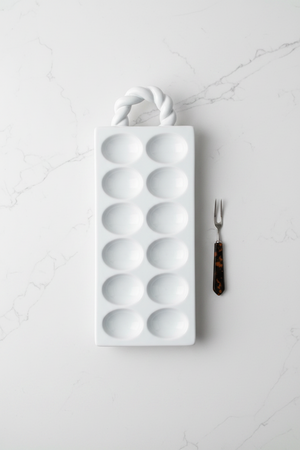 White deviled tray with a handle on a white background with serving fork