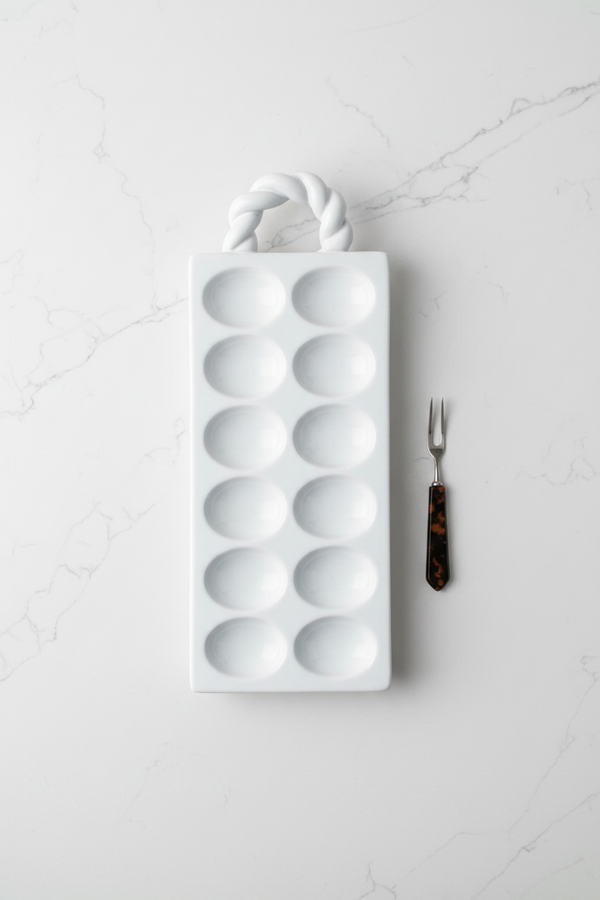 White deviled tray with a handle on a white background with serving fork