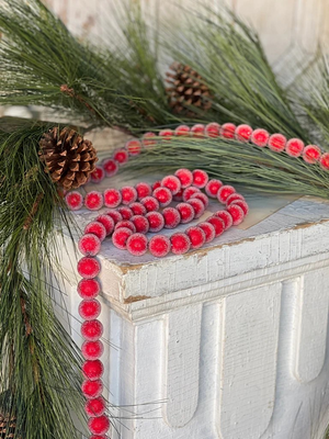 Frosted red bead garland draped over a white wooden chest with long-needle pine branches and pinecones.