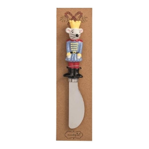 A novelty cheese knife with a nutcracker mouse handle, mounted on a brown cardboard backing. The mouse handle is decorated with a yellow crown, a blue and white striped jacket, red pants, and black boots, holding a silver-colored metal blade.