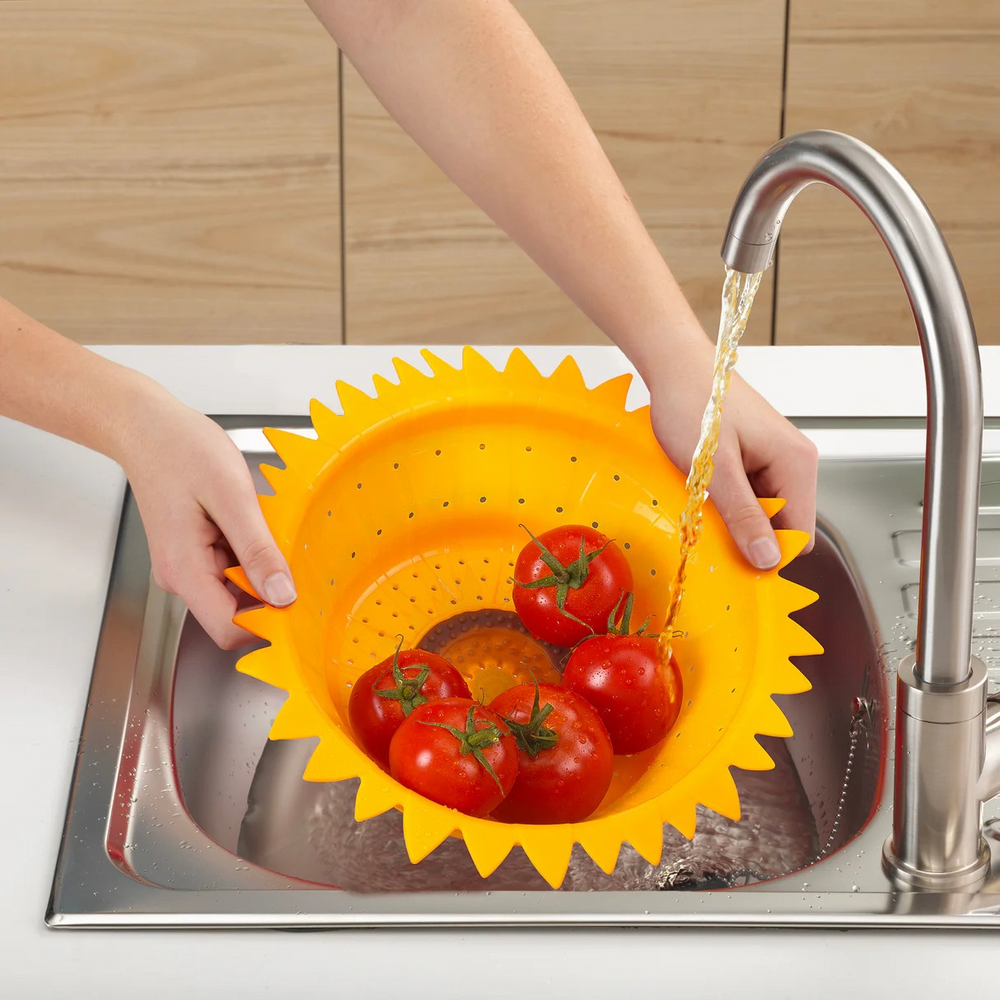 Person washing tomatoes in a yellow colander under running water in a kitchen sink.