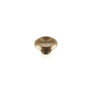 A single round Le creuset knob in a light gold finish, featuring the 'LE CREUSET' brand name printed on its top surface, set against a plain white background.