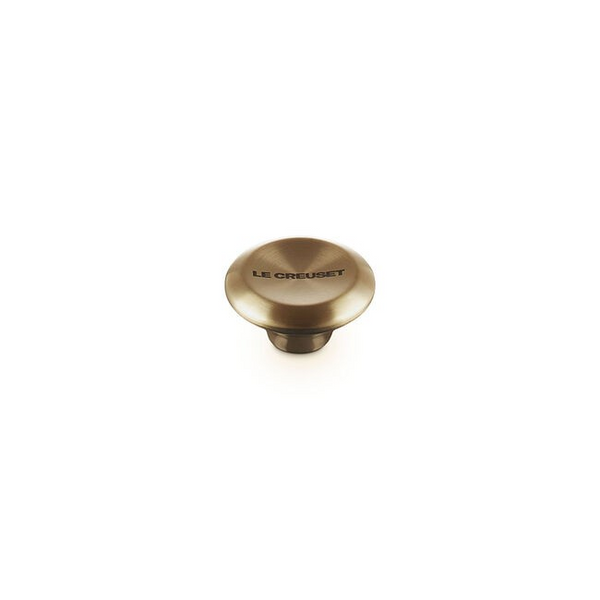 A single round Le creuset knob in a light gold finish, featuring the 'LE CREUSET' brand name printed on its top surface, set against a plain white background.