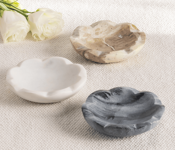 Three marbleized stone bowls in white, gray, and beige on a textured surface with white flowers.